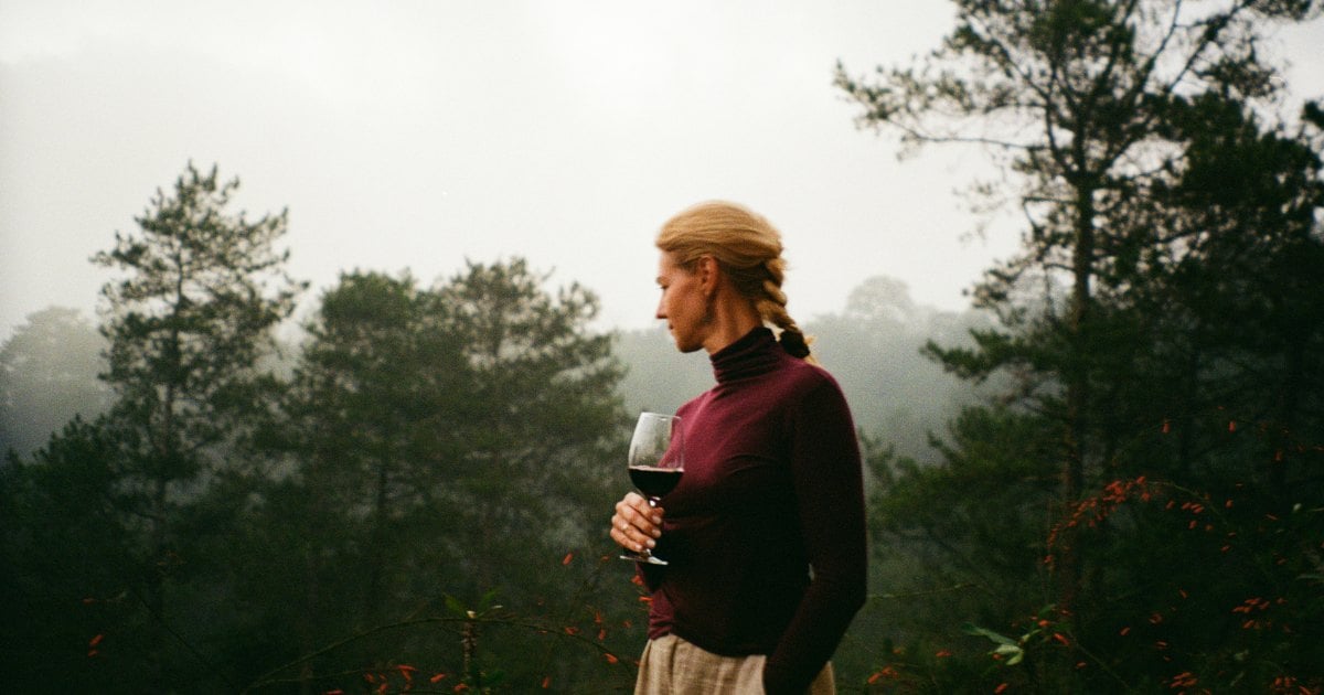 Woman in a burgundy turtleneck holding a glass of red wine on a misty forested terrace