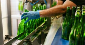 Gloved hand arranging green glass bottles on a beverage bottling line