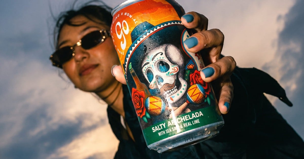 A woman in sunglasses holds a can of Go Brewing Salty Lime AF Chelada non-alcoholic beer toward the camera
