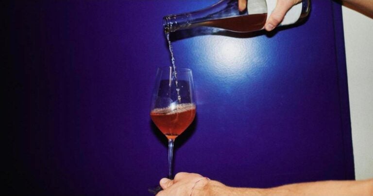 Non-alcoholic rosé poured into a wine glass against a blue wall